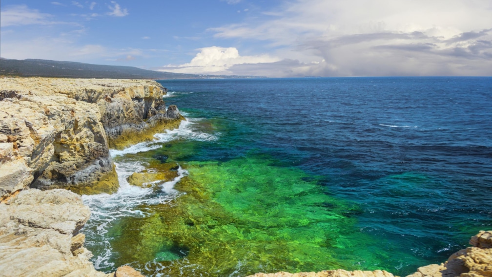 Rocks that lead into the sea, with a blue sky and land in the distance.