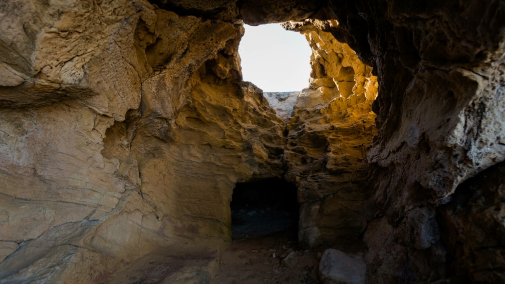 A rocky cave with a hole near the top, where you can see the sky.