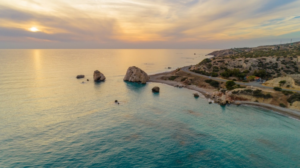 A landscape image of the sunset, the ocean, and land nearby with a road.