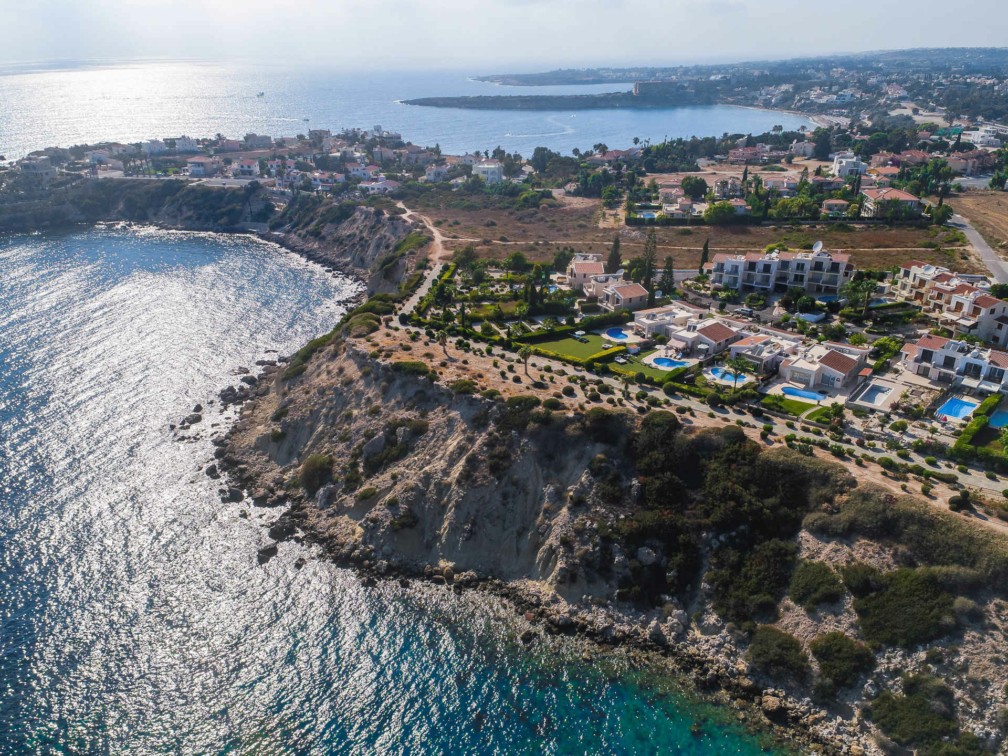 High angled photo of the sea, with a cliff face next to it and buildings on top of the cliff.