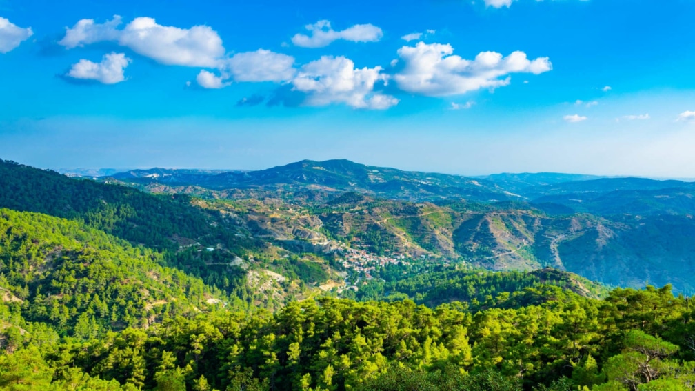 Landscape of the Troodos mountains, with a blue sky and clouds in the background.