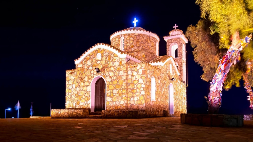 A stone church building, with a lit up cross on the top.