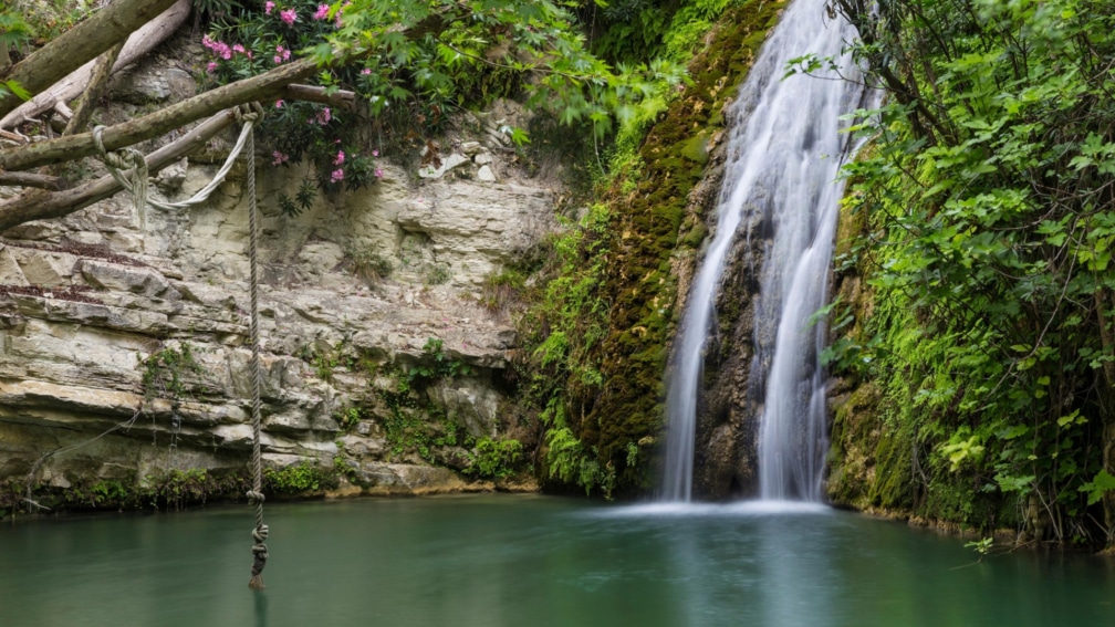 A cove, with a waterfall leading into a pool, and a rope swing hanging from a branch.