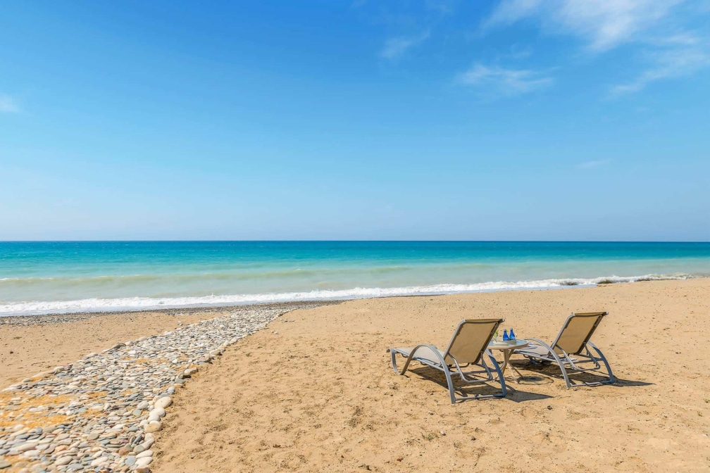 Two deck chairs on a beach facing the sea