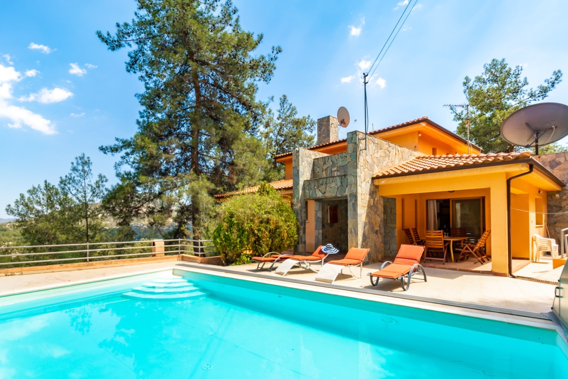 Exterior of the pool at one of Ezoria villas in Cyprus with the terracotta villa and trees in the background