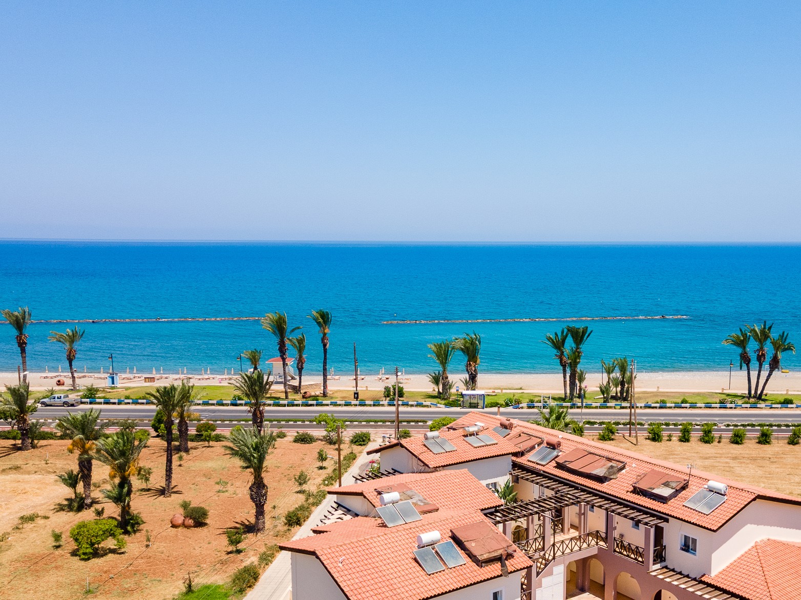 An image of the sea in the background, surrounded by palm trees. Villas are in the foreground.