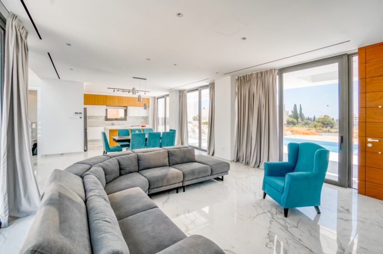 The stunning interiors of the living room space at one of the larger Ezoria villas in Cyprus with a spacious corner couch and the open-plan kitchen