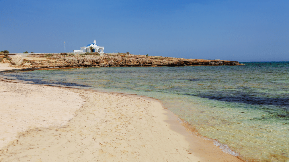 A photo of the beach, with sand and the sea. In the background is a building.