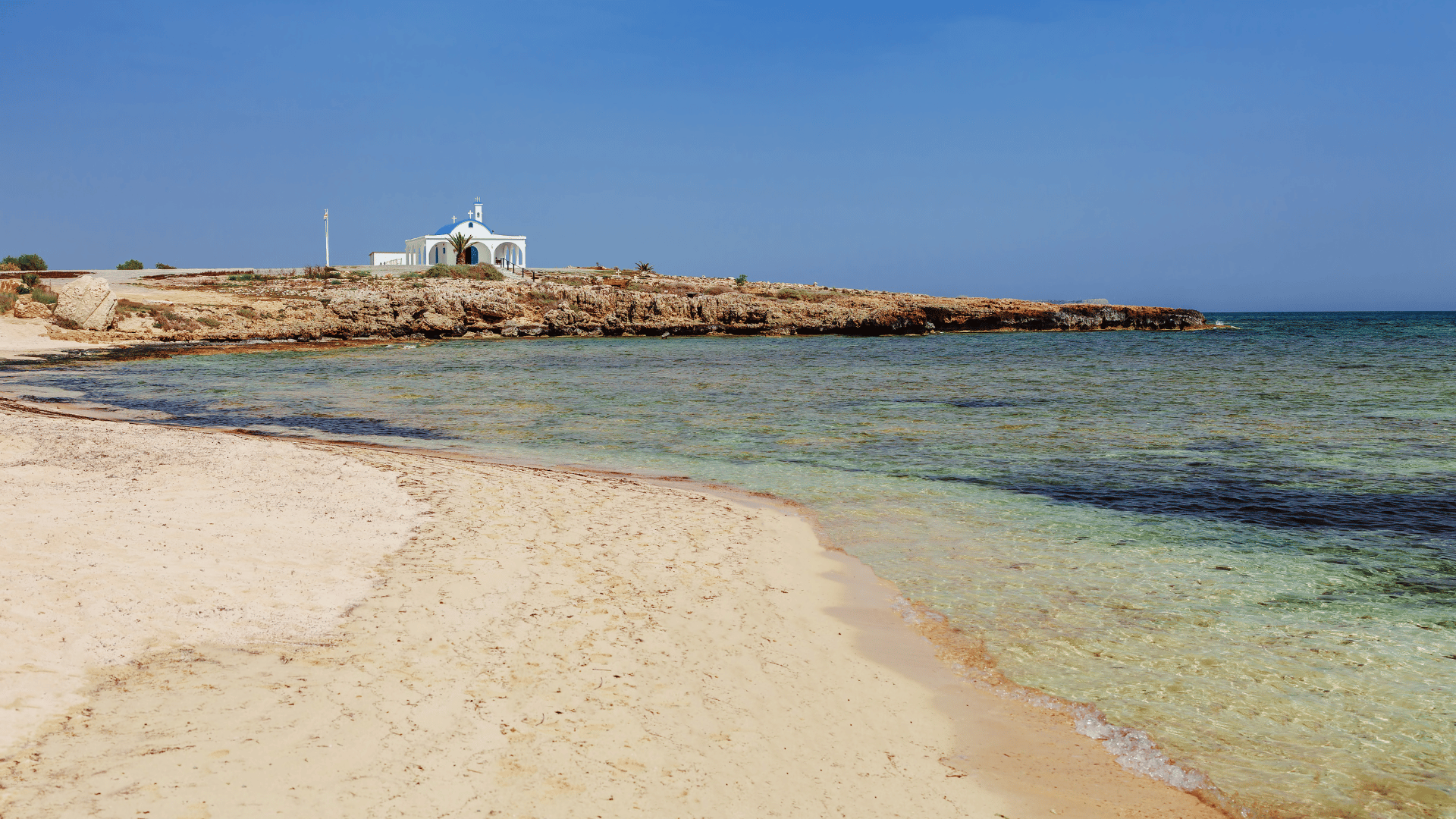 A photo of the beach, with sand and the sea. In the background is a building.