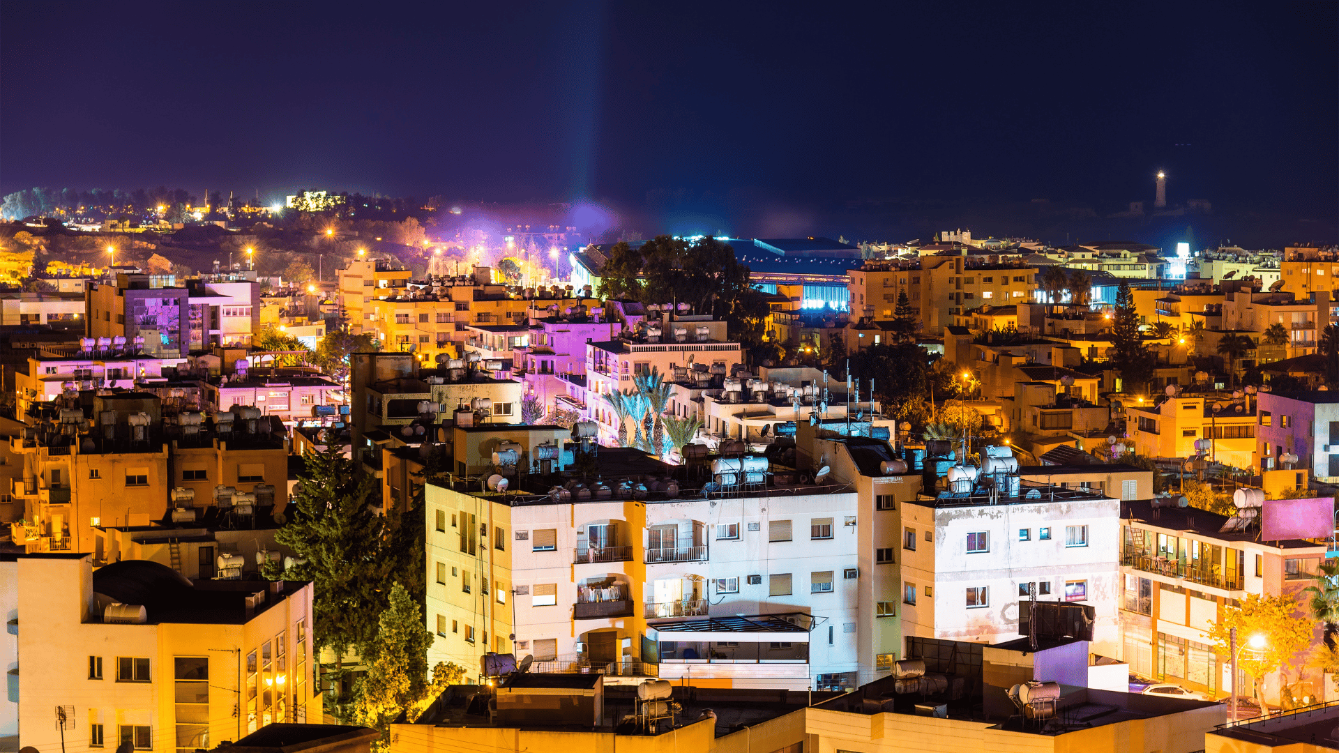 A skyline image of Paphos in the nightime, including apartment buildings and palm trees.