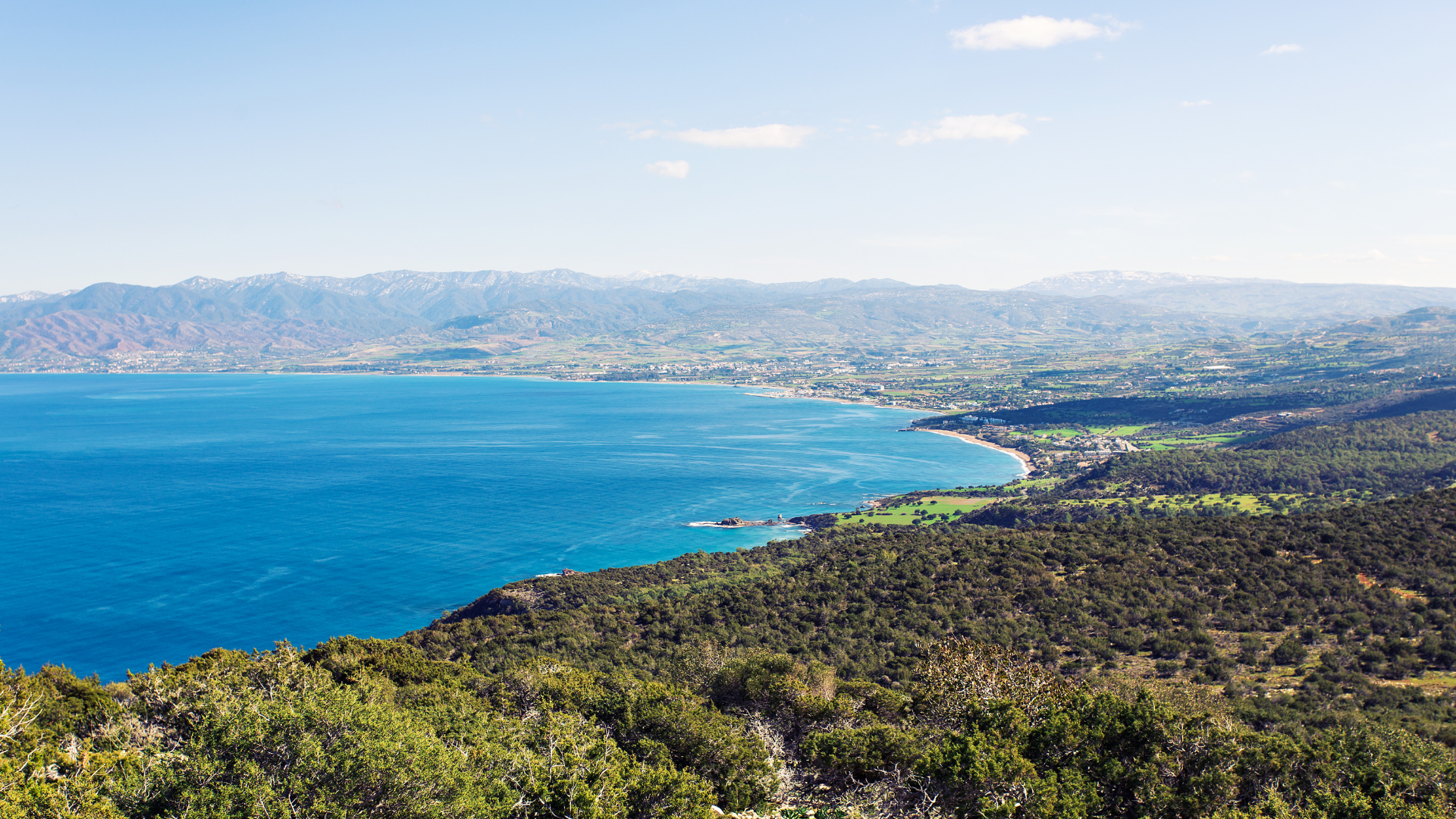 A landscape of the sea, next to land and mountains in the distance.