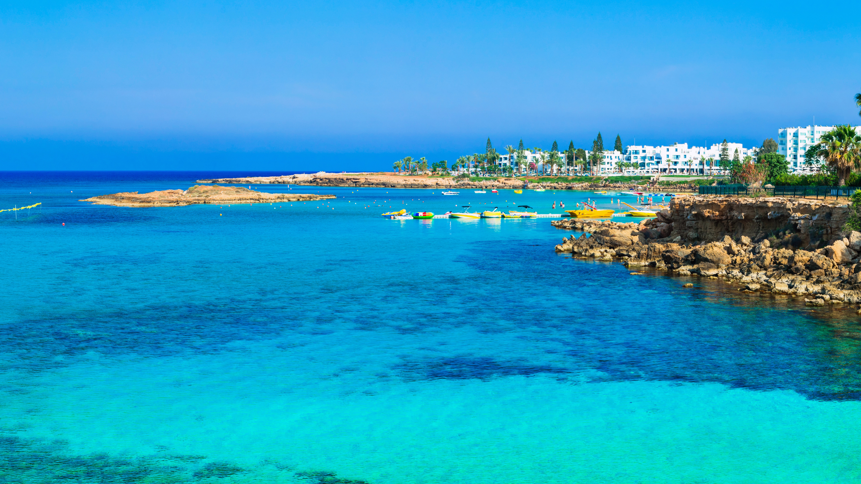 The blue sea with some boats in. Surrounding the sea are rocks and apartment blocks