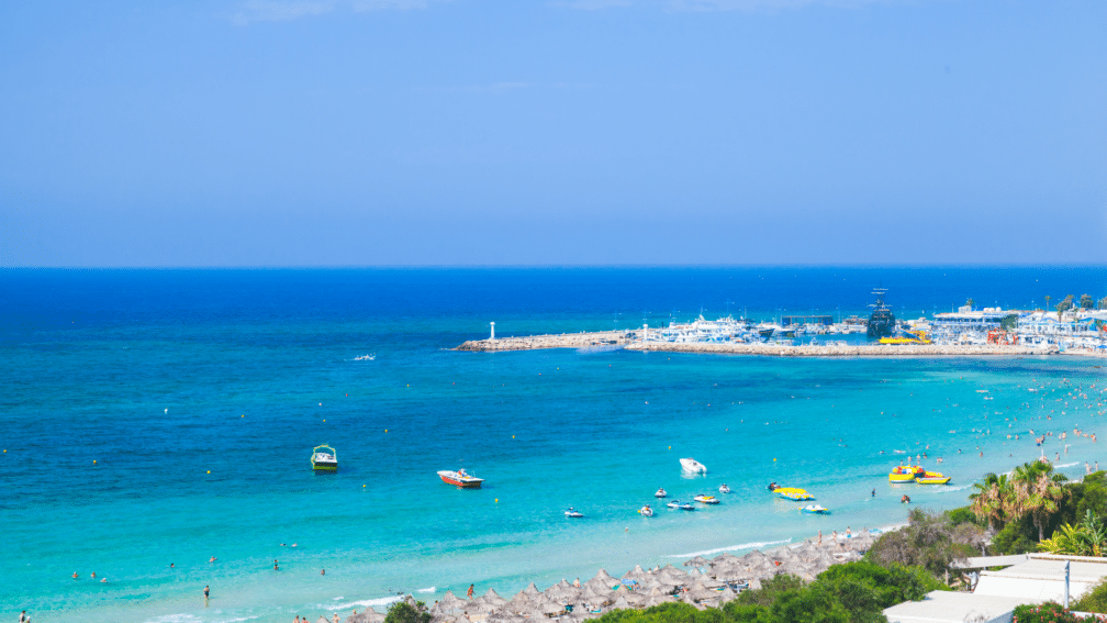 A photo of the sea with boats on. A lighthouse and harbour is in the background.