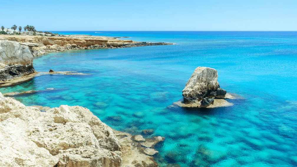 A photo of the ocean surrounded by rocks, with another rock in the middle of it.