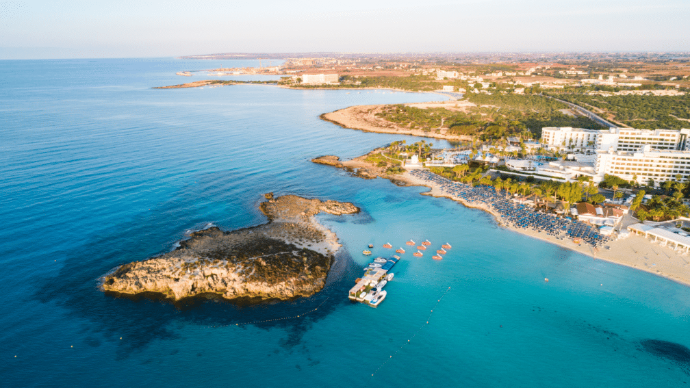 A high angle photo of Cyprus, including the sea, the beach and some buildings on the island.