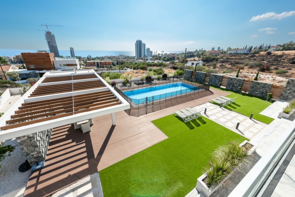 A birds eye view photo of the outside of a villa, with grass, deckchairs and a swimming pool.