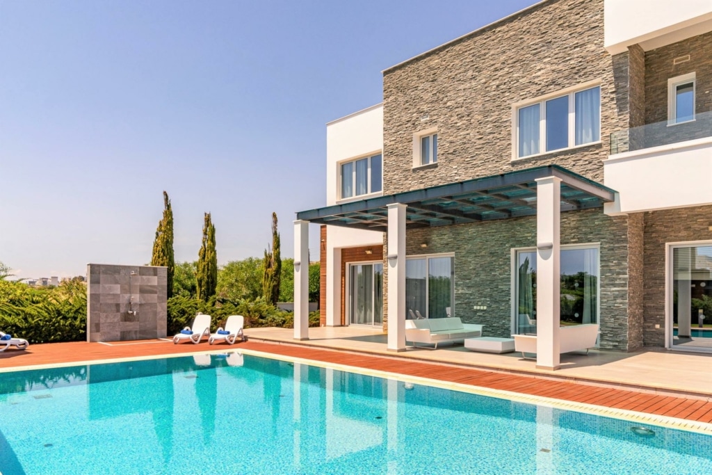 outside of a villa, with a pool, two deck chairs and outdoor shower