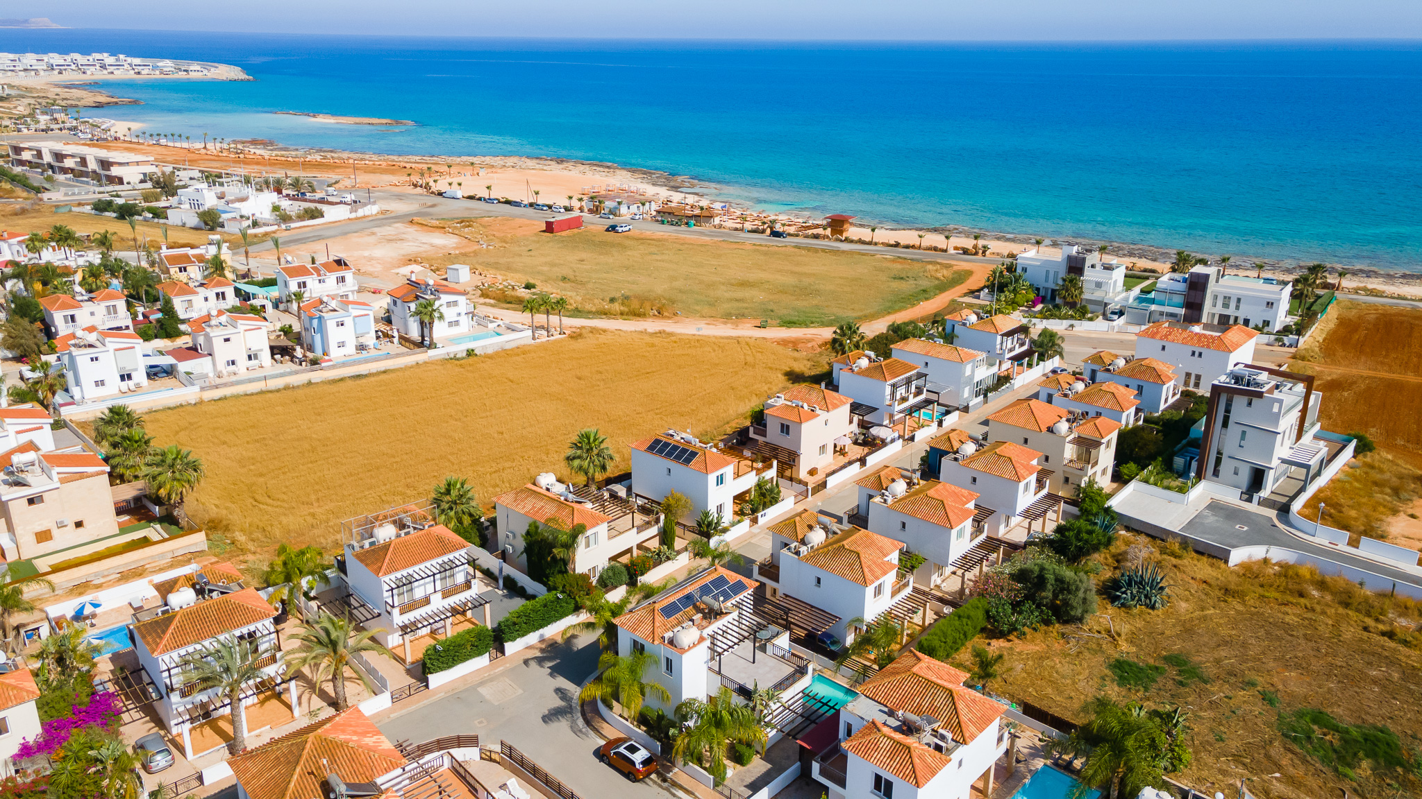 A high angle photo of villas surrounding a field. There are pools by the villas and palm trees.