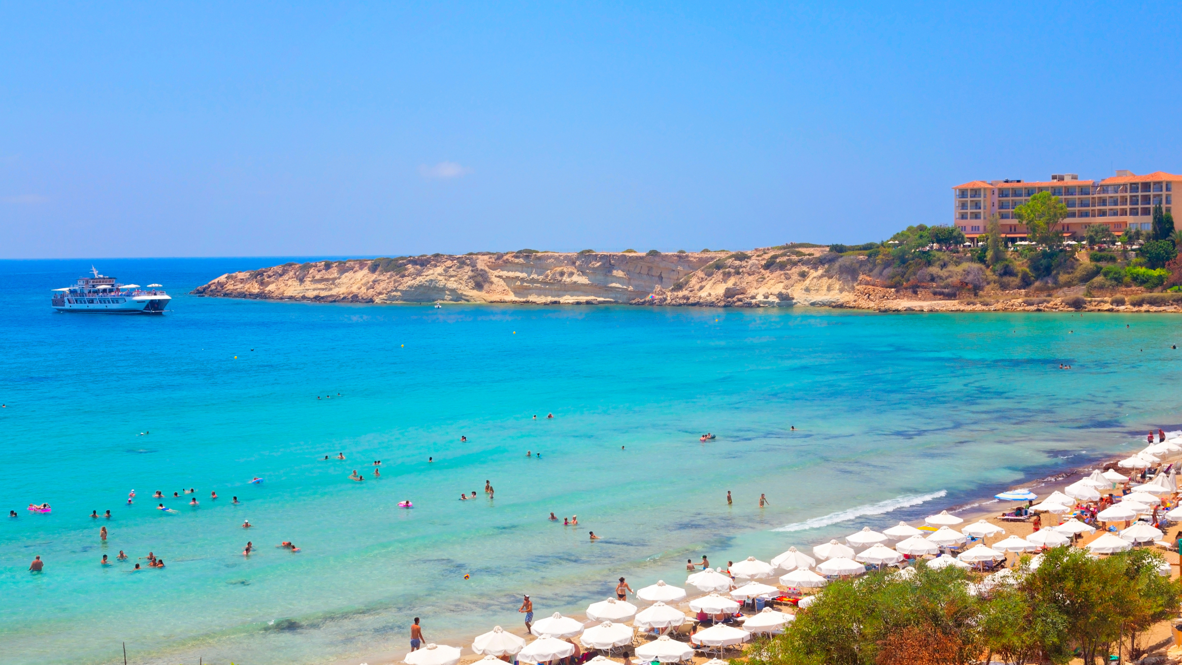 A photo of a beach and the sea. The beach has umbrellas on and there are people in the sea.